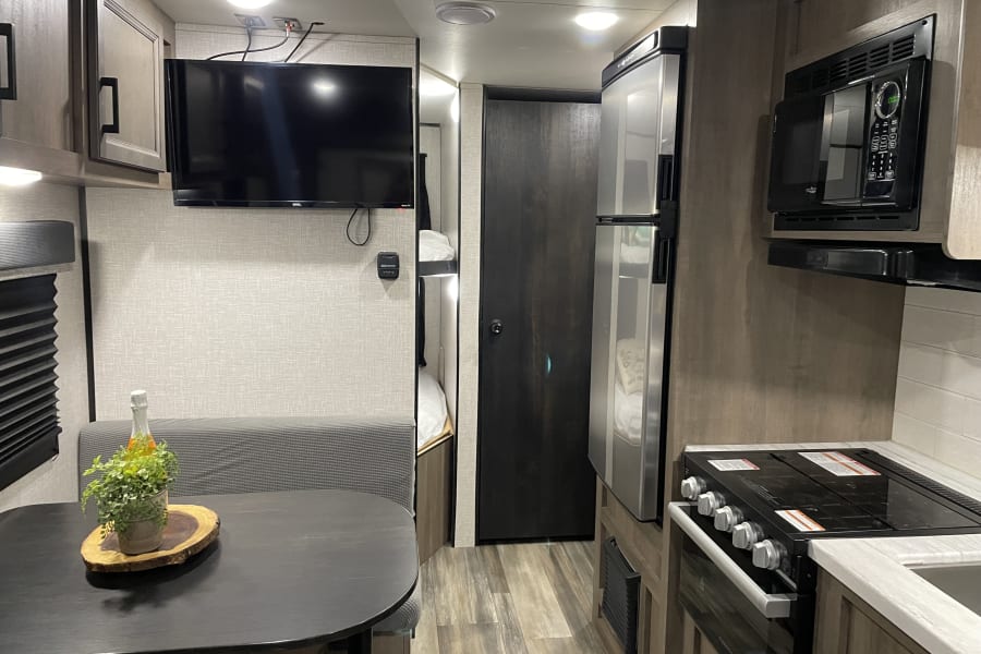Spacious RV rental interior: equipped kitchen (microwave, stove, fridge), dining booth, TV, and comfy bunk beds.