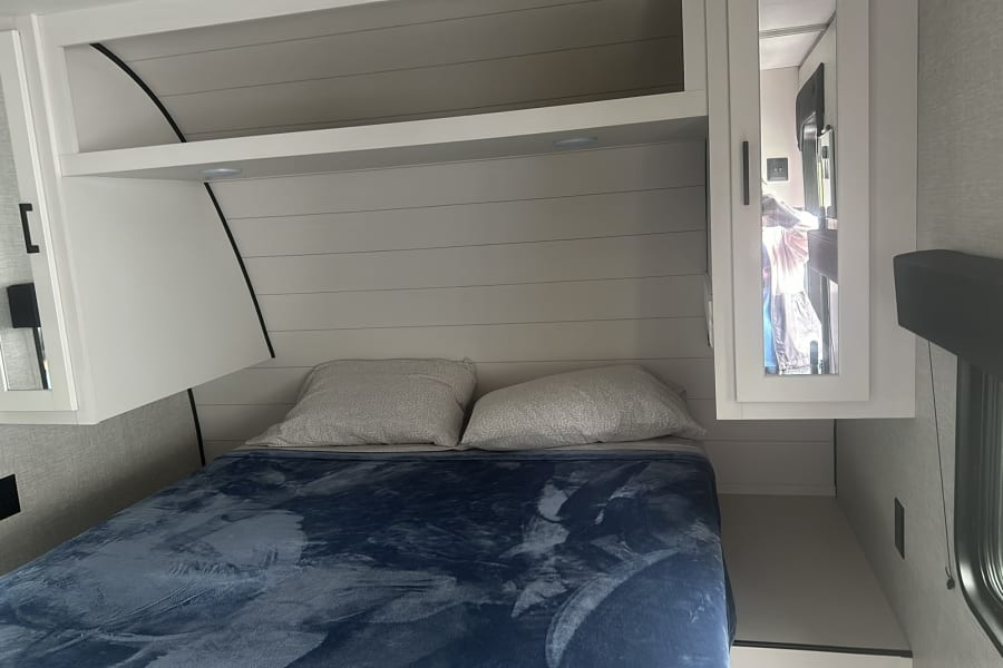 Relaxing RV rental bedroom showcasing a comfy bed with blue blanket, white shiplap accent wall, and built-in storage.