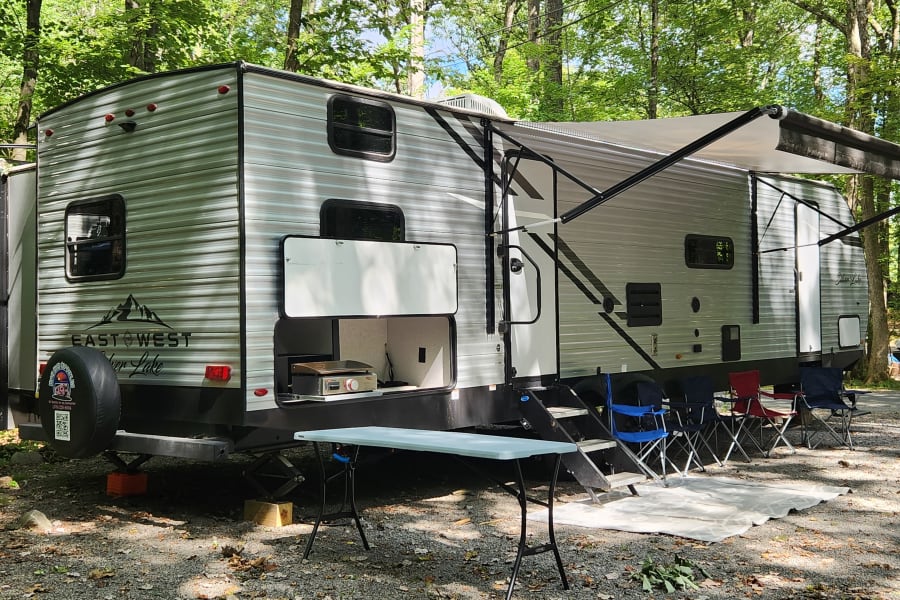 This RV rental at a shady campsite offers an outdoor kitchen, extended awning, and chairs for relaxing.