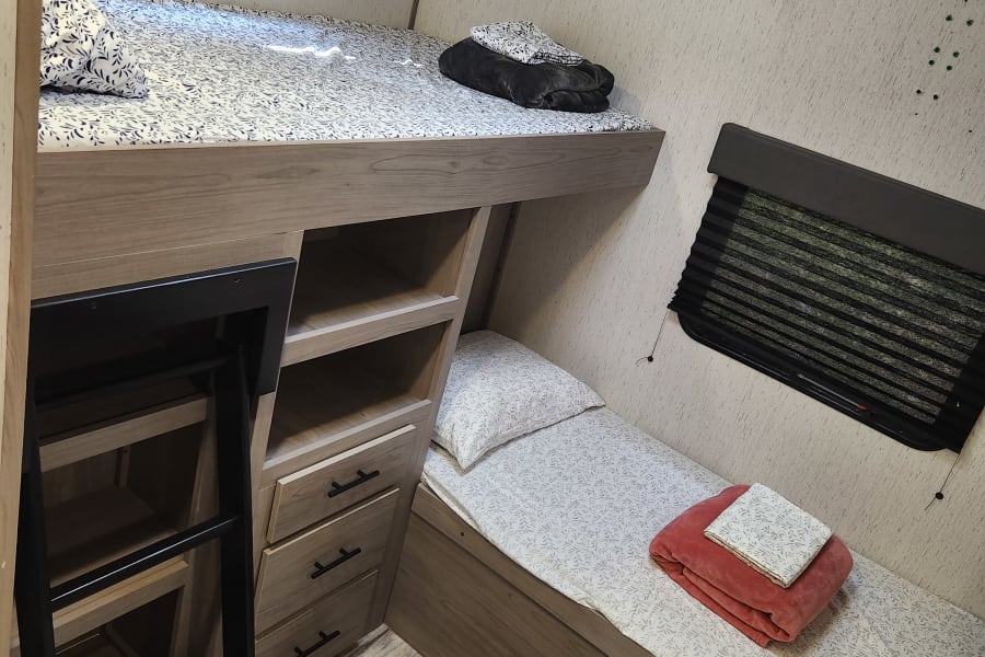 Inside an RV rental: a comfortable bunk area featuring upper & lower beds, built-in storage, and windows with blinds.