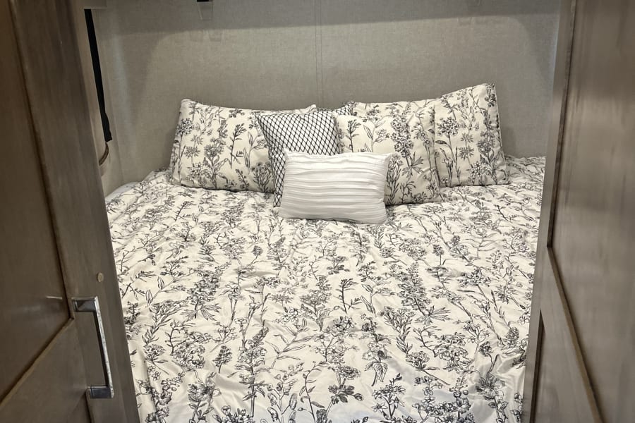 Step into this comfortable rv rental bedroom, featuring floral bedding, spacious overhead cabinets, and soft lighting.