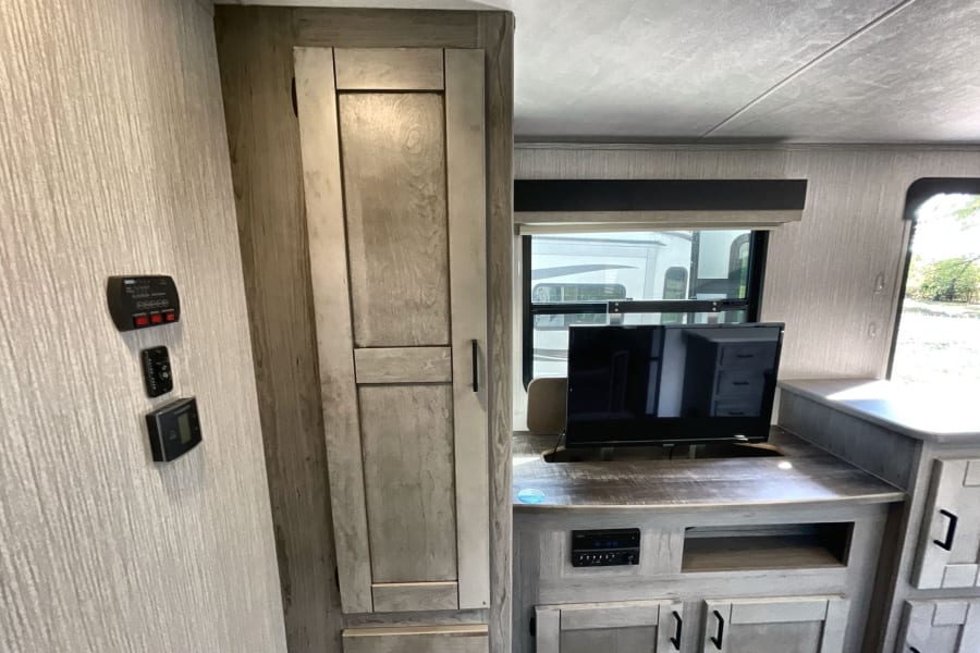 Modern rv rental interior featuring wall controls, a TV, and sleek wood-toned cabinets with ample storage.