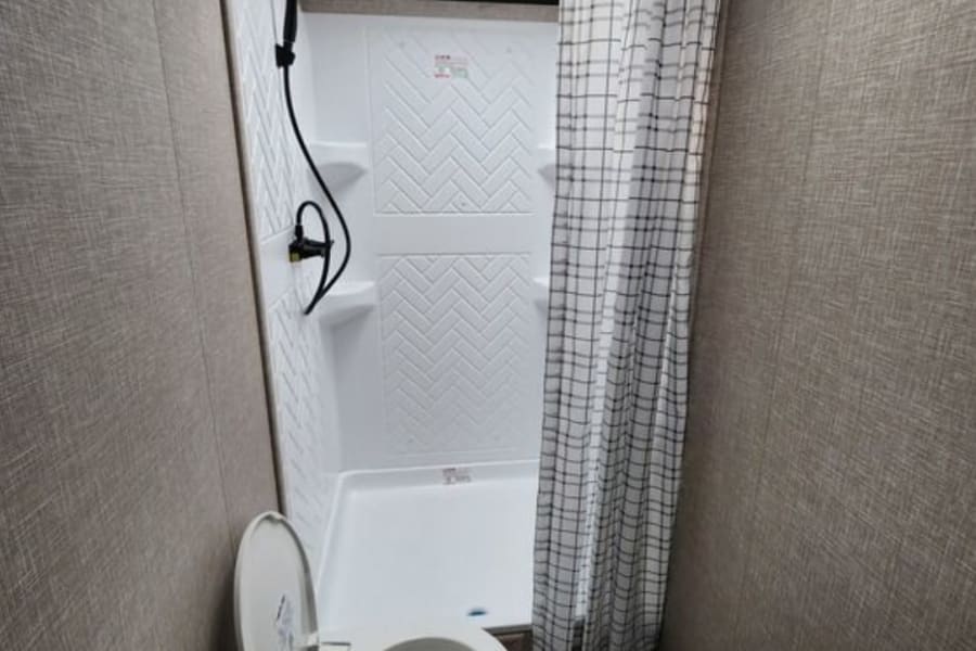 This functional RV rental bathroom features a toilet, shower with patterned curtain, and textured walls, perfect for mobile living.