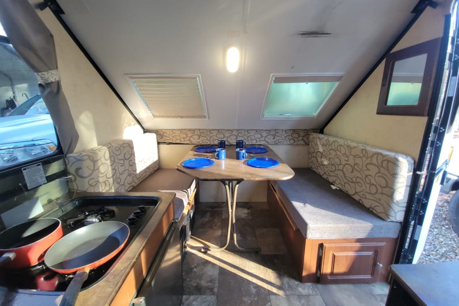 Inside an rv rental pop-up camper, showing a dining area with table and benches, plus a small kitchen stove.
