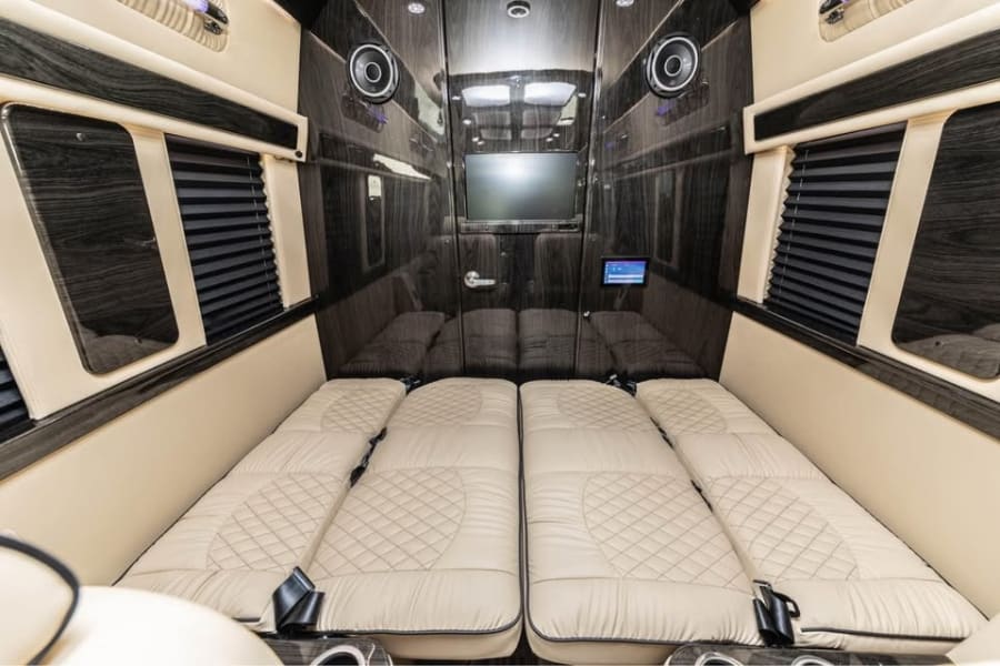Experience comfort in this rv rental! Features fold-down beds, TV, sleek wood paneling, and cream upholstery.