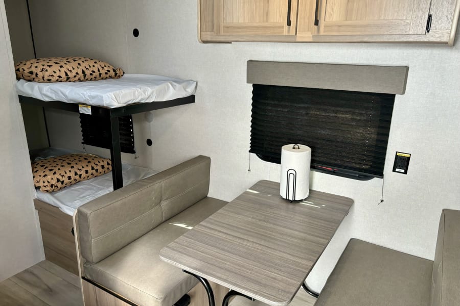 RV rental interior: bunk beds, dinette with table, overhead cabinets, and light wood tones.