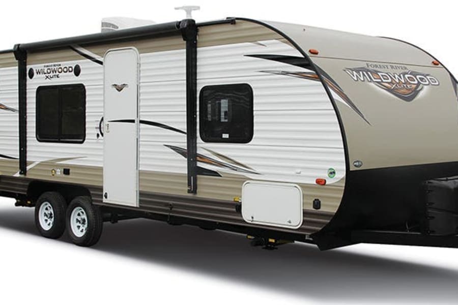This beige and white travel trailer, perfect for an RV rental, features an awning and multiple windows for mobile adventures.