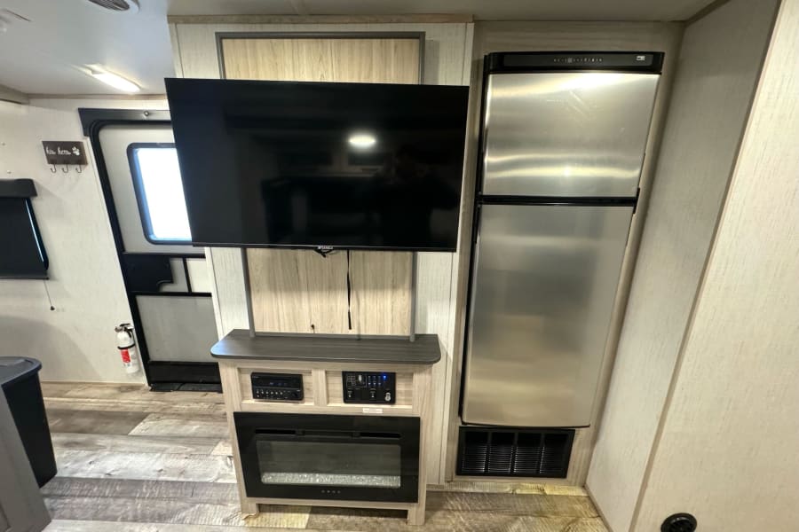 Cozy RV rental living space featuring a large TV, electric fireplace, and full-size refrigerator. Ready for your adventure.