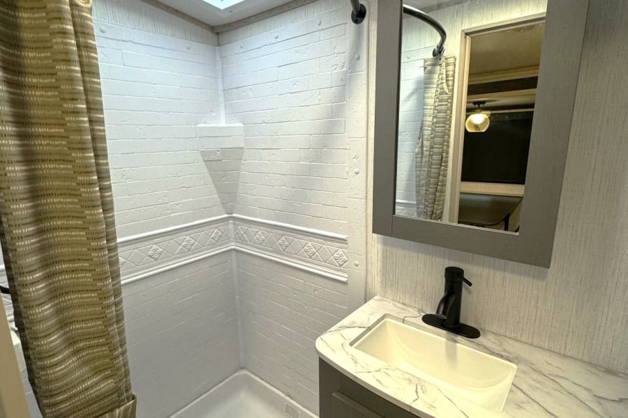 RV rental bathroom with a modern shower, skylight, and vanity. Ideal for comfortable travel and camping.