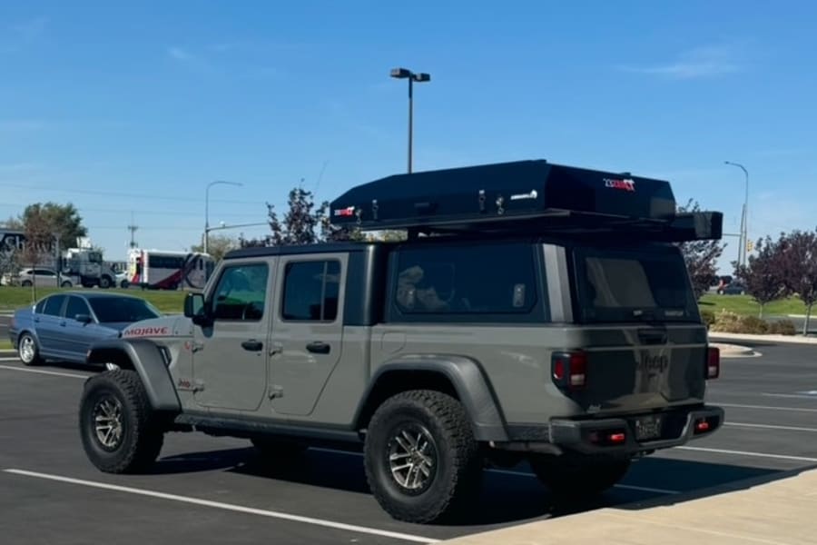 This gray Jeep Gladiator, equipped with a rooftop tent and camper shell, offers a unique alternative to an RV rental for your next outdoor adventure.