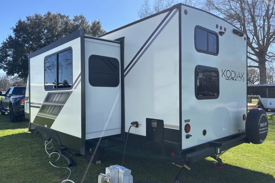A white Kodiak Ultra-Lite RV rental with its slide-out extended, powered up and ready for camping on a grassy site.