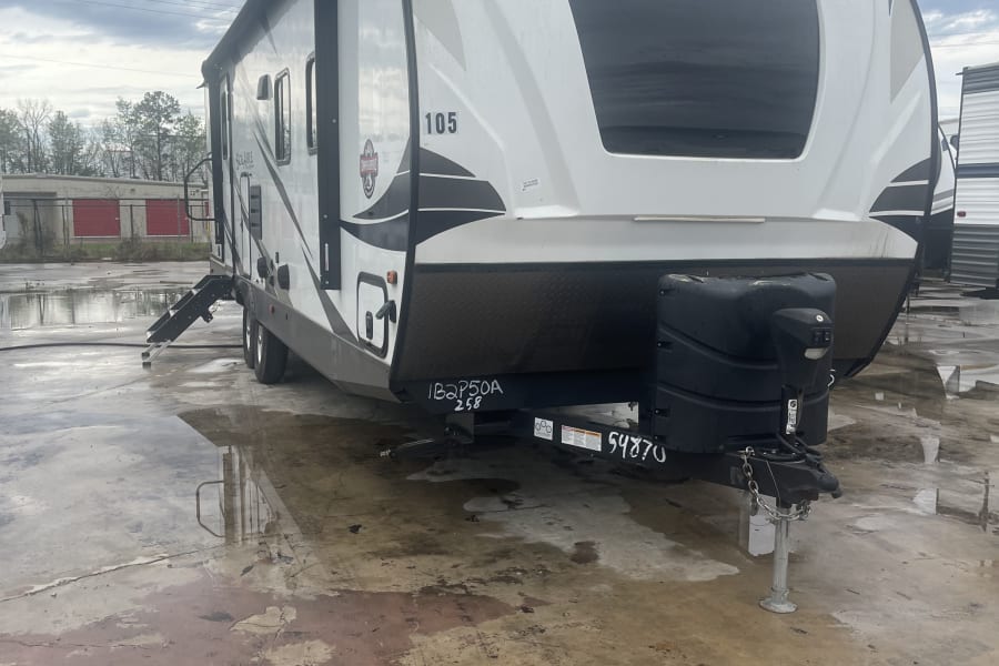 White Solaire travel trailer RV rental, parked on a wet lot, showing the front and side view.