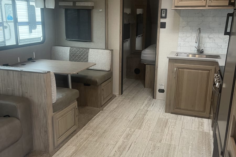Spacious RV rental interior, showcasing a bright dinette, kitchen area, and a glimpse of the bedroom. Modern and clean design.