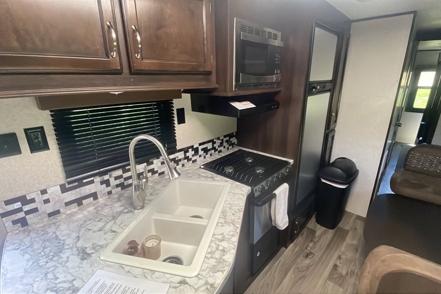 This RV rental features a well-equipped kitchen: double sink, stove, microwave, fridge, and ample storage.