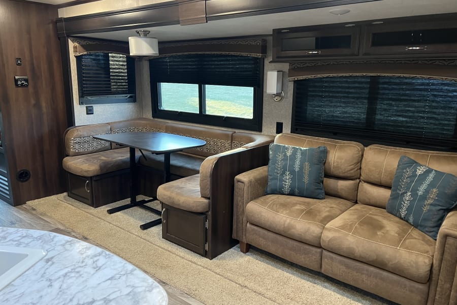 Spacious RV rental living area with comfy U-shaped dinette, sofa, and ample natural light. Ideal for family trips.