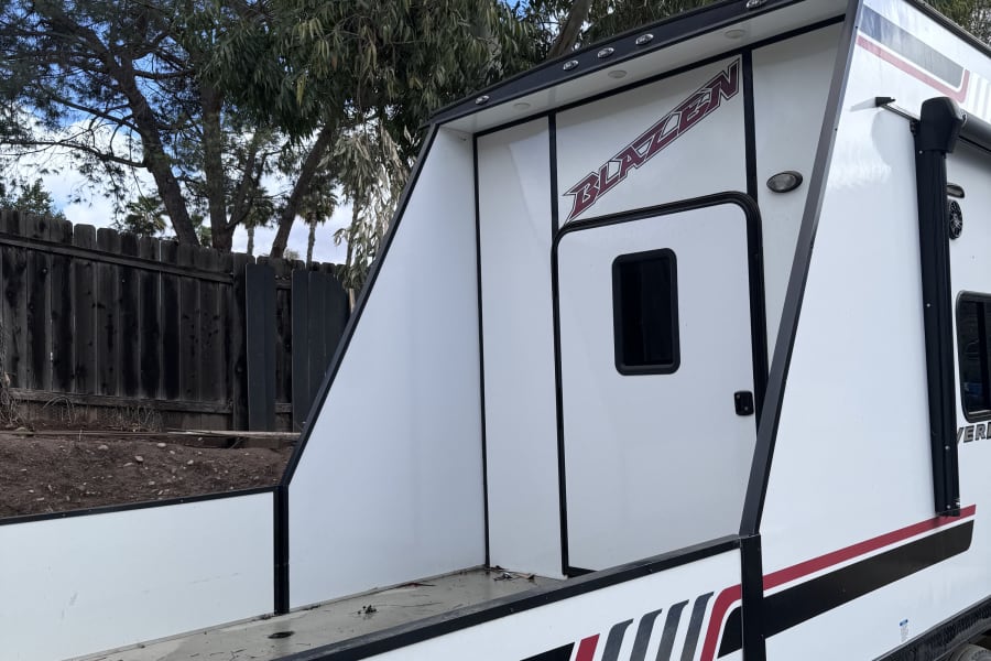 Close-up of a white Blazen fifth-wheel toy hauler, ideal for an rv rental, with black and red graphics and multiple axles.