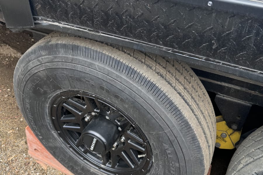 RV rental's dually tire on a red leveling block, showing tire dry rot & black diamond plate skirting.
