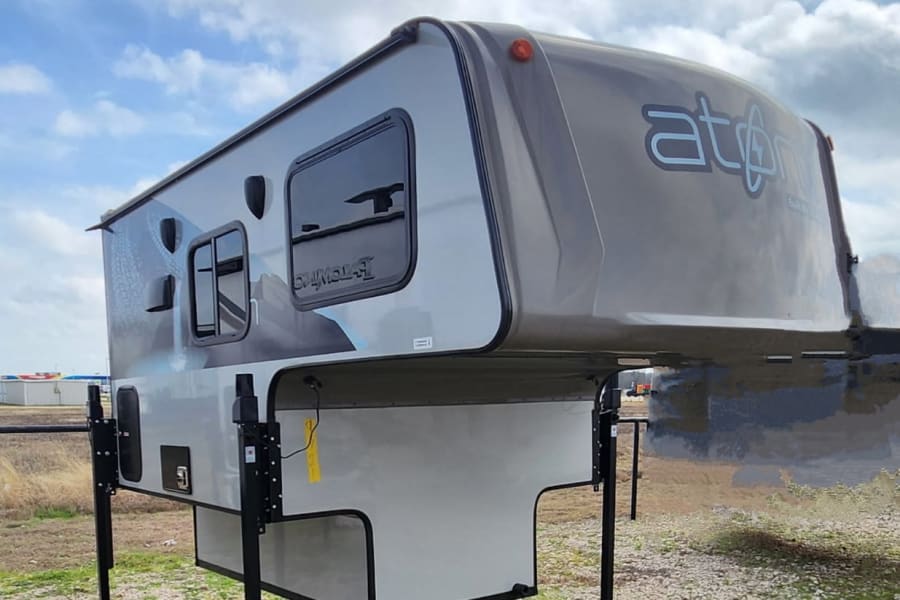 Grey Atom truck camper, a versatile RV rental option ready for outdoor adventures. Equipped with sturdy jacks.