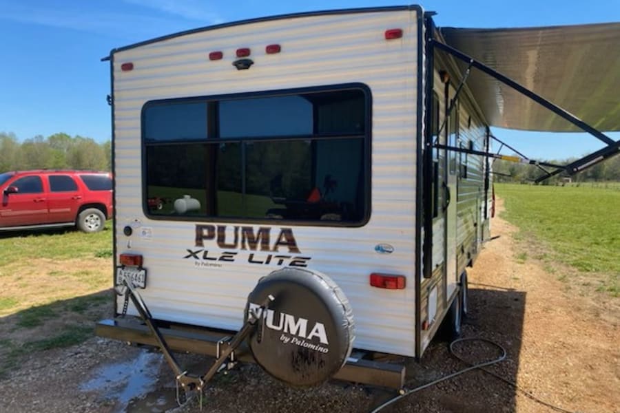 A white Puma XLE Lite travel trailer RV with awning extended, perfect for your next rv rental or camping trip.