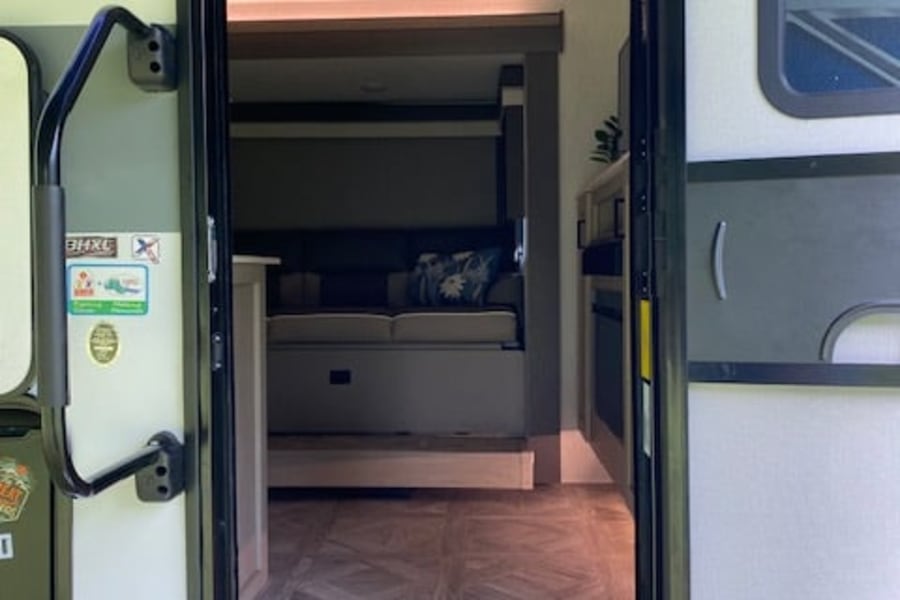 Step inside this RV rental! The view through the open door shows patterned flooring, a step, and a cozy interior living area.