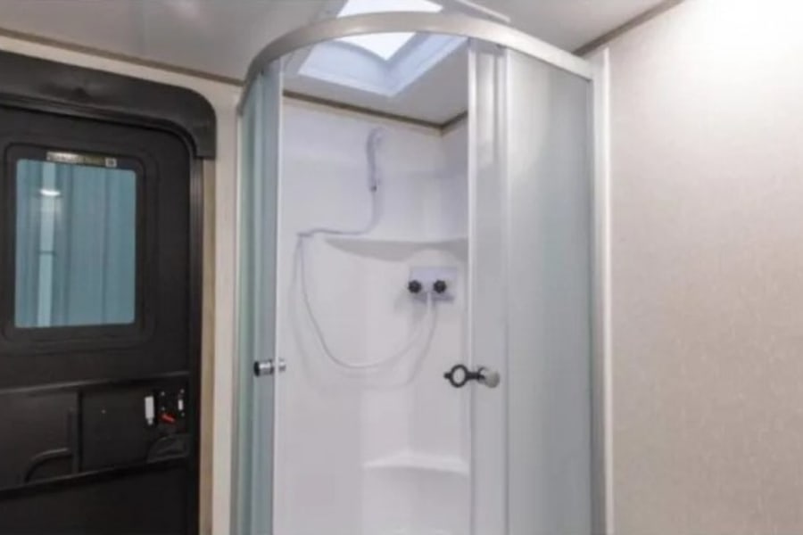 RV rental interior features a compact, curved glass shower cabin with skylight and a dark entry door. Efficient use of space.