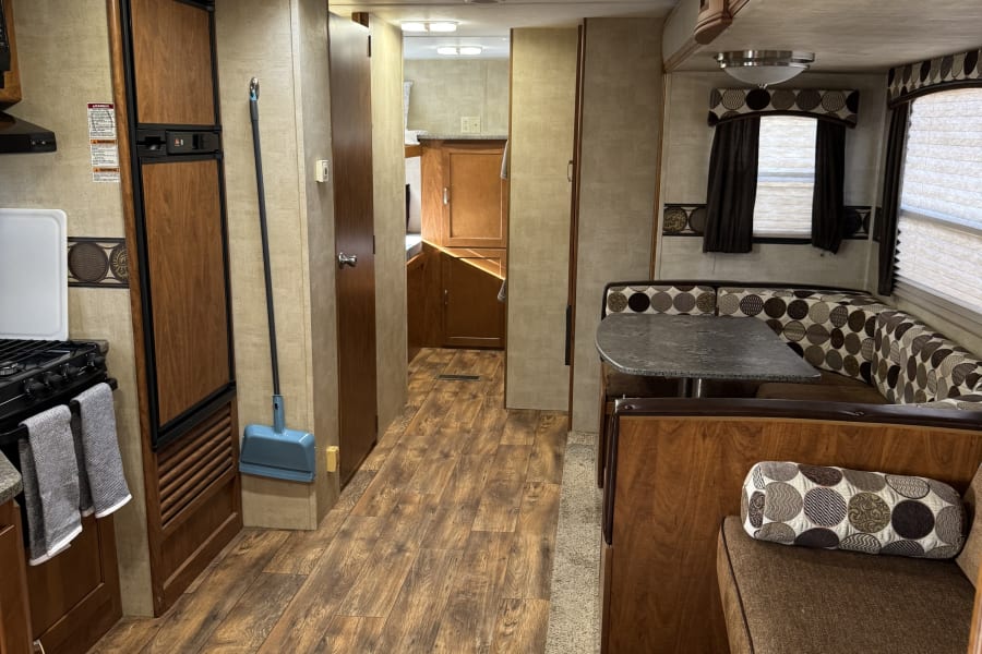 RV rental interior: kitchen with stove & fridge, dining dinette with patterned cushions, & wood-look floor in the hallway.