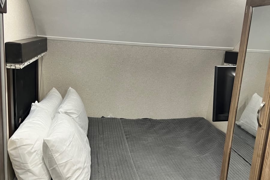 Compact RV rental bedroom featuring a cozy bed, overhead lighting, and built-in storage.