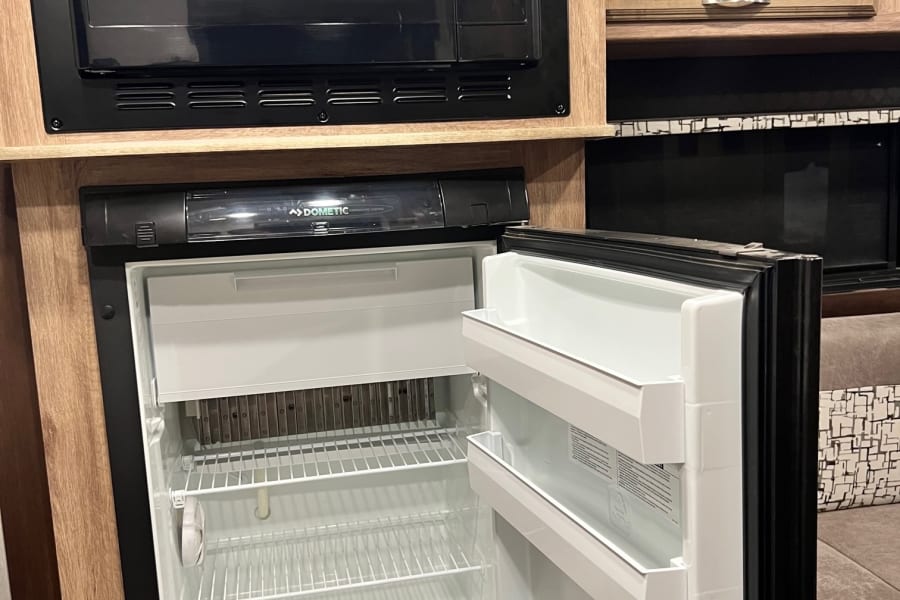 Compact kitchen in an RV rental, showing a High Pointe microwave and an open Dometic refrigerator with shelves.