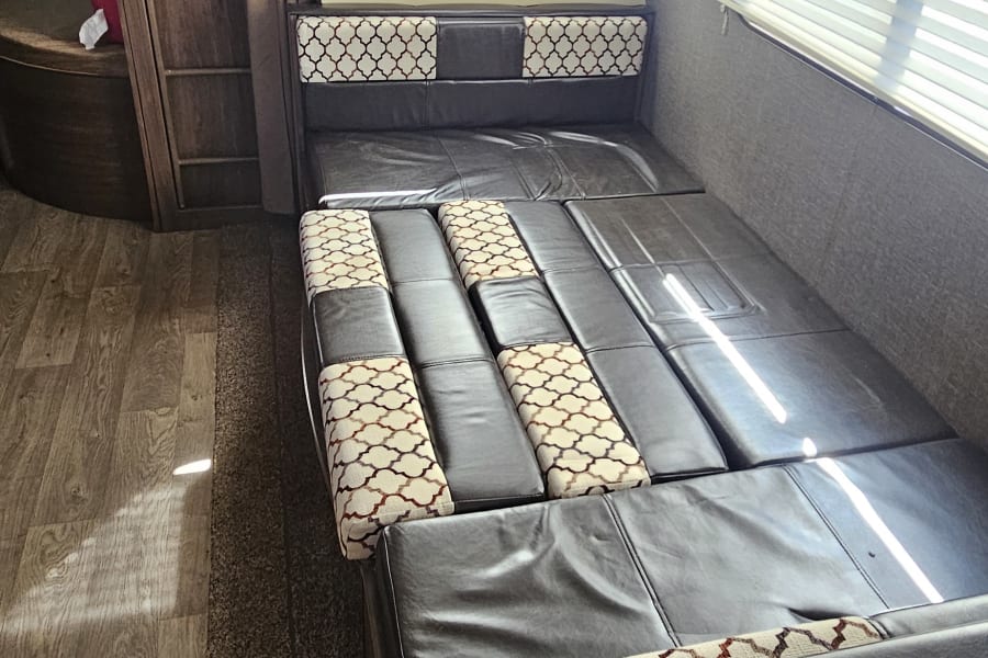 RV rental interior showing a dinette converted to a bed, bunk beds, and windows. A cozy space for travel adventures.