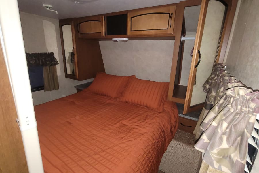 Comfortable RV rental bedroom with orange bed, overhead cabinets, and closet space, perfect for your travel adventure.