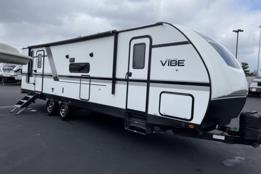 A large, modern white travel trailer RV with black accents, 'Vibe' model, with its steps deployed, perfect for an RV rental adventure.