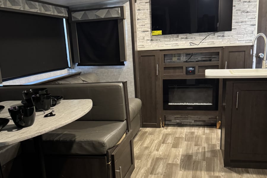 Inside an RV rental, showcasing a comfortable dining booth, entertainment center with TV & fireplace, and modern decor.