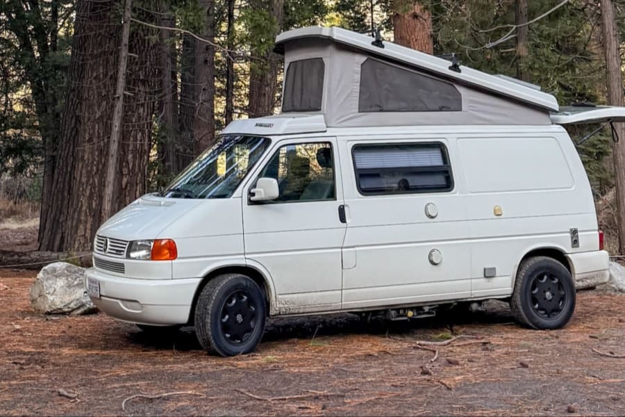 This white pop-top camper van RV rental is set up for camping in a beautiful forest clearing.