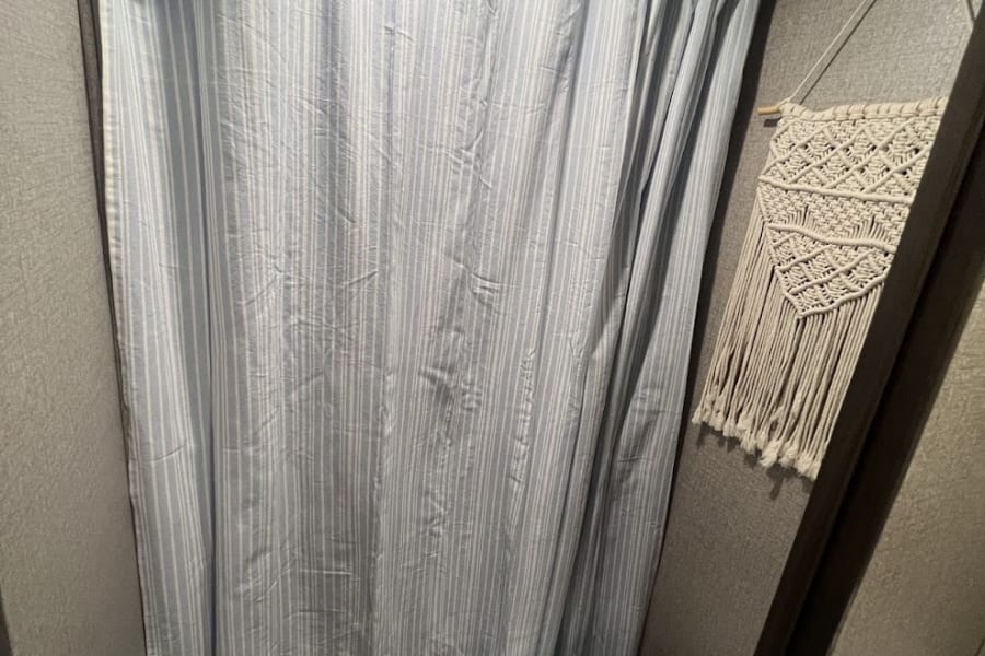 Compact RV rental bathroom features striped shower curtain, toilet, and macrame wall decor.