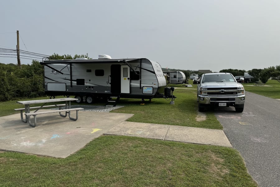 RV rental travel trailer and pickup truck set up at a grassy campsite with a picnic table, offering a comfortable outdoor stay.