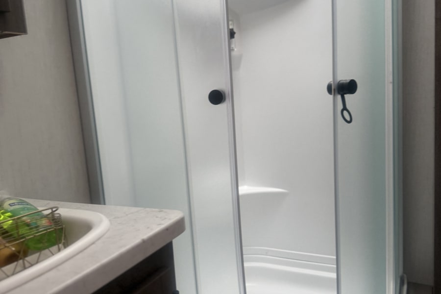 This RV rental bathroom features a corner shower with frosted glass doors and a sink vanity for your convenience.