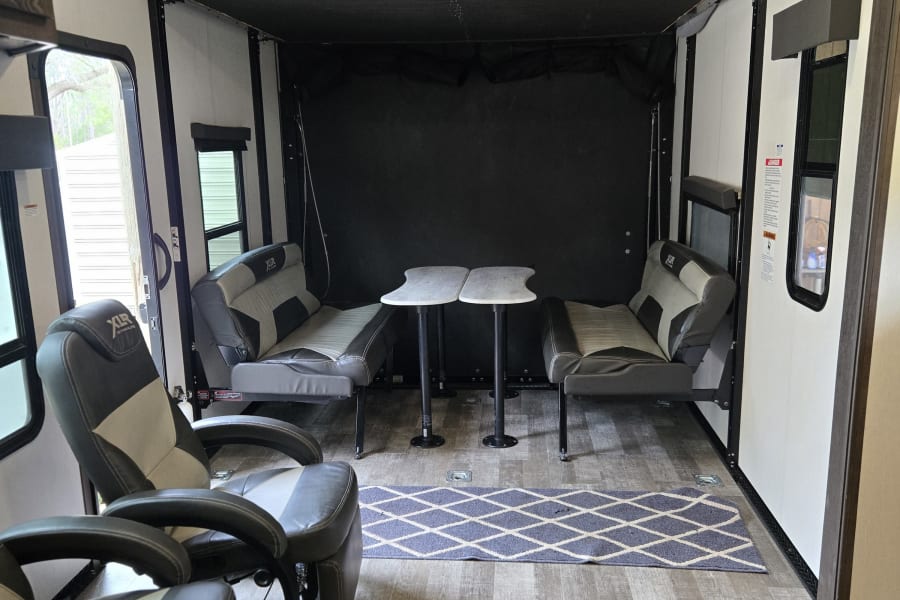 RV rental interior features recliners, convertible seating/dining with tables, and a drop-down bunk bed.