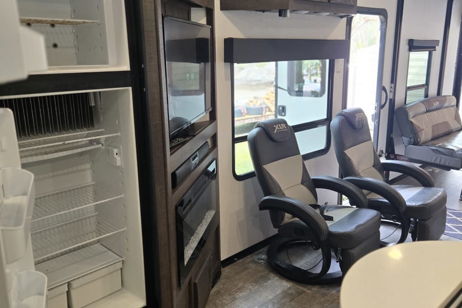 Spacious RV interior with an open fridge, entertainment system, and comfy recliners, perfect for your next RV rental.