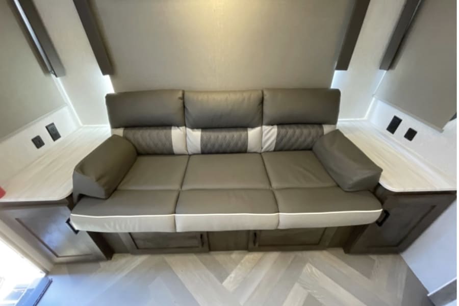 Spacious gray sofa with side tables & outlets in an RV rental interior. Perfect for relaxing during your trip.