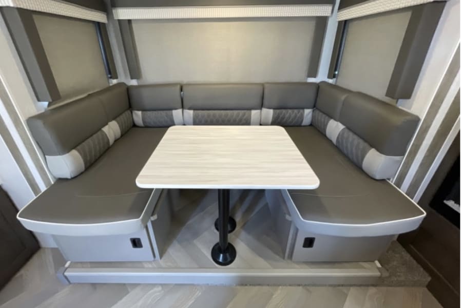 U-shaped RV rental dinette with comfortable gray seating & table, perfect for meals & relaxation.