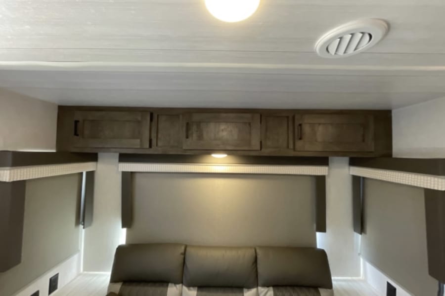 RV rental interior: Light-filled living space with dark wood overhead cabinets, comfy sofa, and window shades.