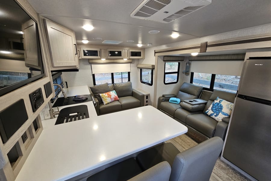 Inside a clean RV rental, featuring a full kitchen, living room with recliners, and dining area. Perfect for travel.