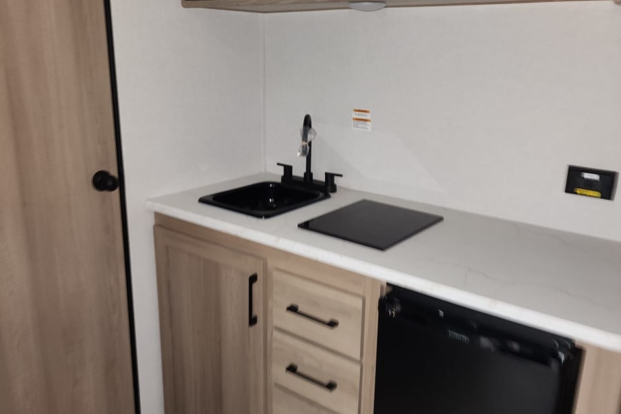 Modern RV rental kitchenette featuring a microwave, sink, cooktop, and under-counter fridge.