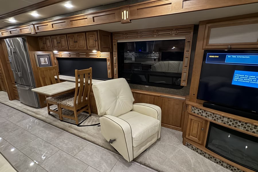 Spacious, modern RV rental interior with kitchen, dining area, cozy recliner, large TV, and fireplace.