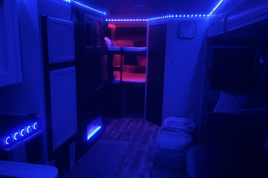 An RV rental's interior glows with blue LED strips, featuring cozy bunk beds with magenta lighting.