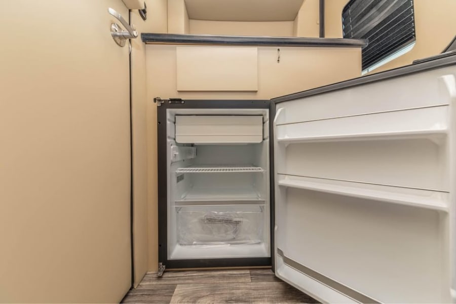 This open, empty mini-fridge in an RV rental kitchen is ready for your food and drinks on the go.