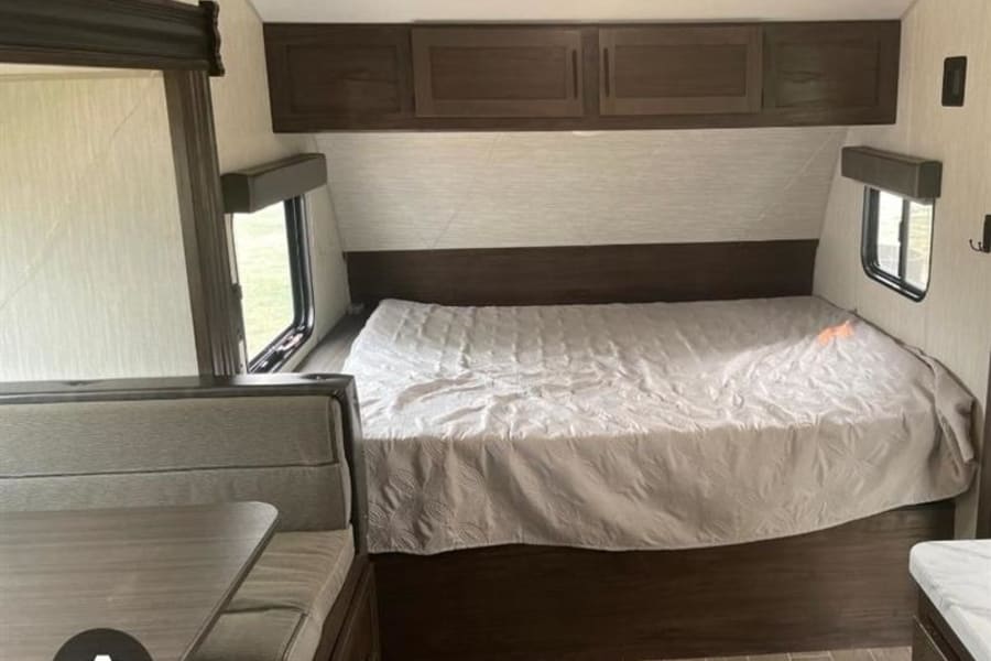 Inside an RV rental: A compact living space with a bed, dinette, and storage. Wood-look flooring. Ready for your adventure.