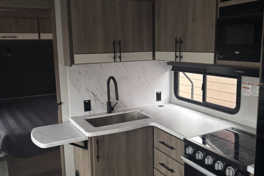 RV rental interior: modern kitchen with wood-grain cabinets, marble-look counters, sink, stove, and microwave.