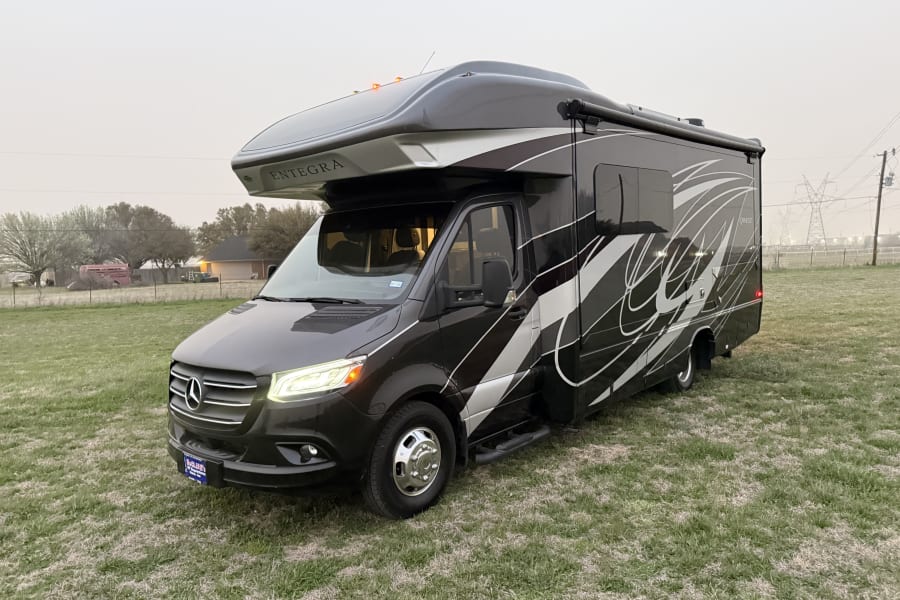 A sleek grey Entegra Qwest Mercedes-Benz Class C RV in a grassy field. Ideal for your next rv rental and luxury travel.