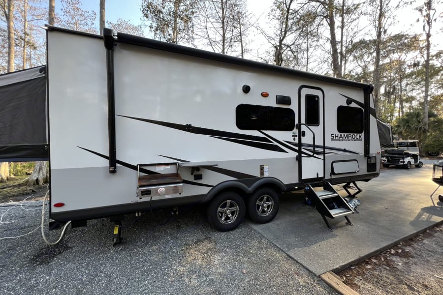 Shamrock Flagstaff travel trailer RV rental with outdoor griddle & steps, perfectly set up at a gravel campsite.
